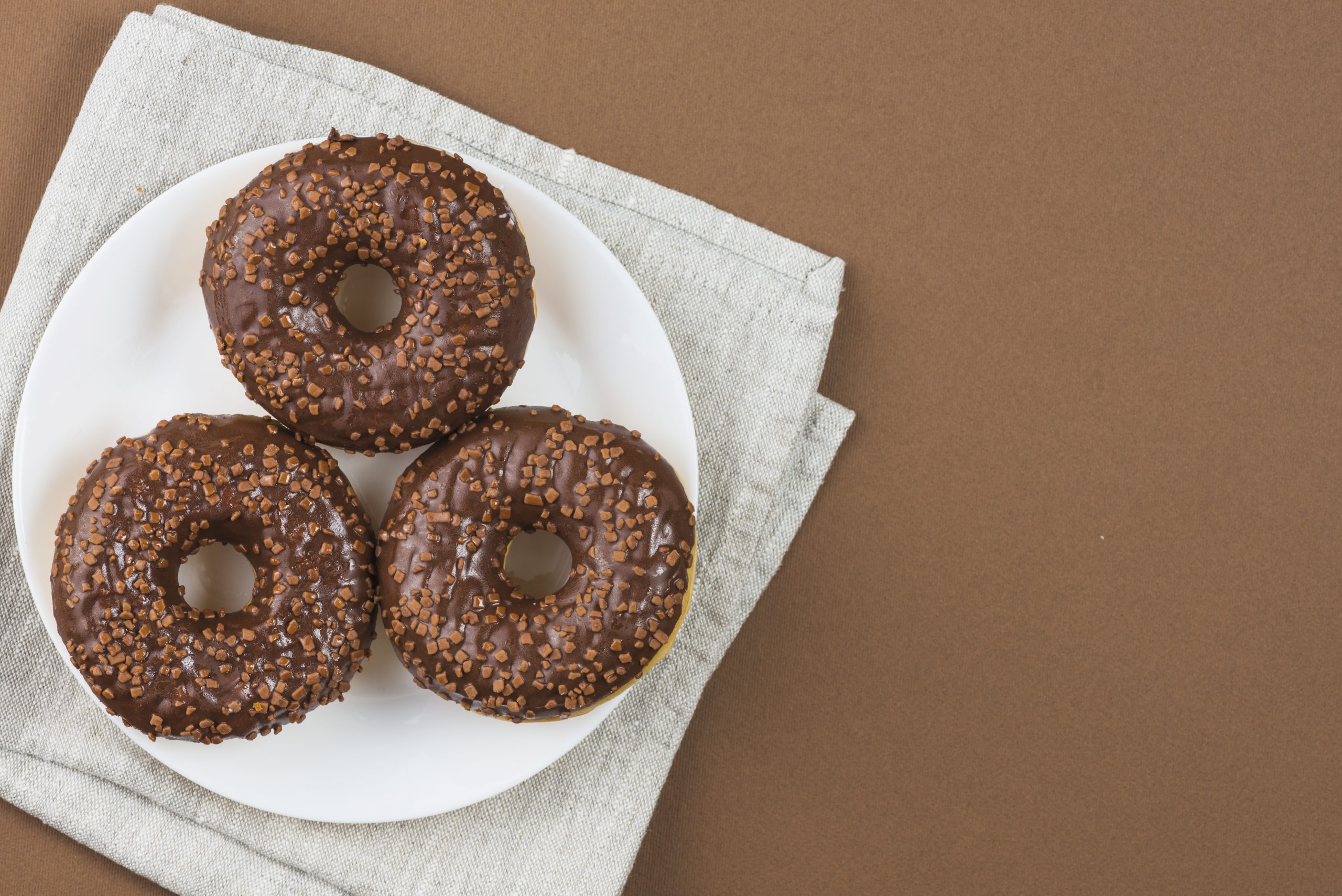 chocolate-glazed-doughnuts-white-plate-gray-cloth-scaled.jpg